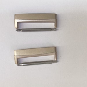 May include: Two gold-toned watch band spring bars. The spring bars are made of metal and have a silver finish.