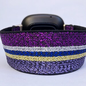 Puede incluir: Una pulsera de reloj de color morado, plateado, azul y dorado con purpurina y base el&aacute;stica negra.