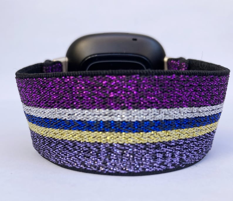Puede incluir: Una pulsera de reloj de color morado, plateado, azul y dorado con purpurina y base el&aacute;stica negra.