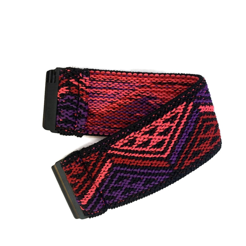 Puede incluir: Un cintur&oacute;n tejido con un patr&oacute;n geom&eacute;trico en tonos de rosa, morado y negro. El cintur&oacute;n tiene una hebilla negra.