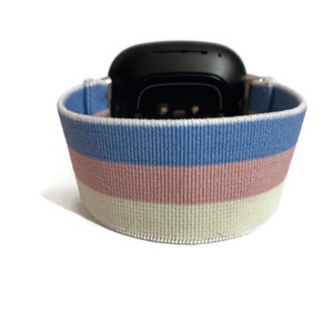 May include: A blue, pink and white striped elastic watch band. The band is made of a soft, stretchy material and is designed to fit a variety of wrist sizes.