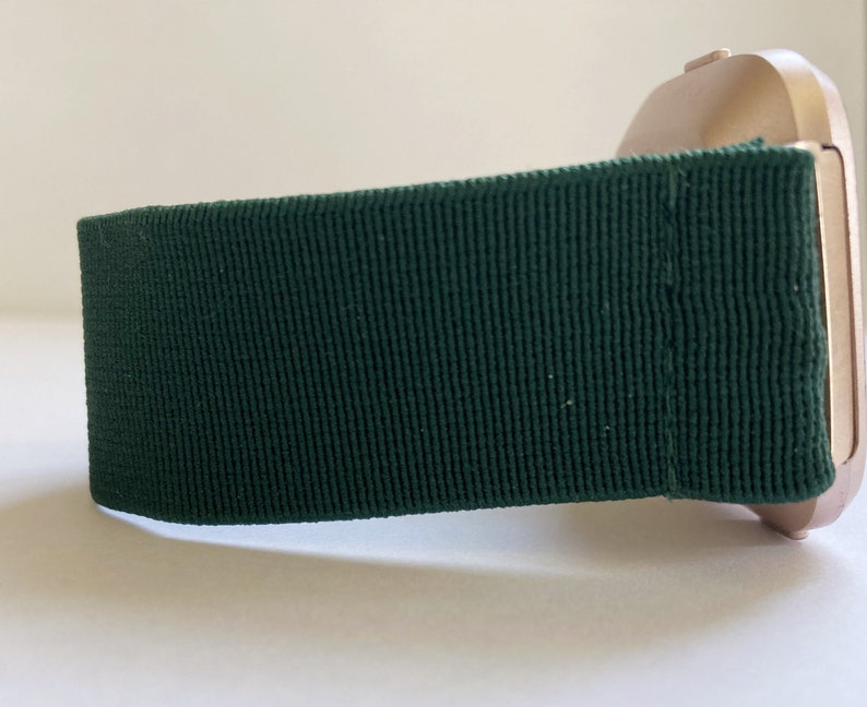 Op de afbeelding: Een goudkleurig horloge met een donkergroene stoffen band. De band is gemaakt van geweven materiaal.