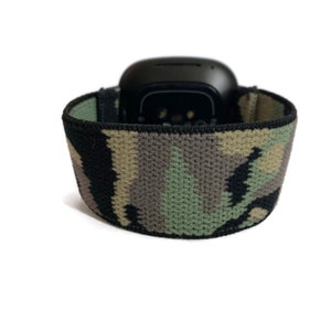 May include: A black smartwatch with a camouflage patterned band. The band is made of a soft, stretchy material.