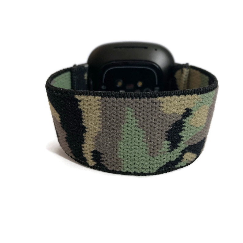May include: A black smartwatch with a camouflage patterned band. The band is made of a soft, stretchy material.