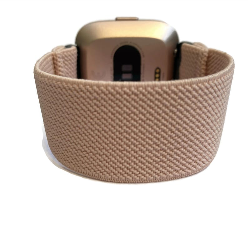 K&ouml;nnte beinhalten: Eine ros&eacute;goldene Smartwatch mit einem beigefarbenen elastischen Armband. Das Zifferblatt der Uhr ist sichtbar und hat einen schwarzen Bildschirm.