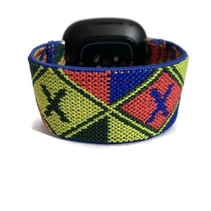 May include: A colorful woven watch band with a blue, red, green, and yellow geometric pattern. The band features a black and white logo.