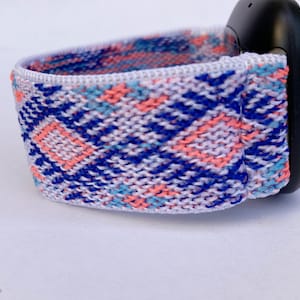 May include: A white woven watch band with a blue, pink, and light blue geometric pattern.