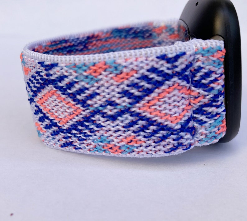 May include: A white woven watch band with a blue, pink, and light blue geometric pattern.