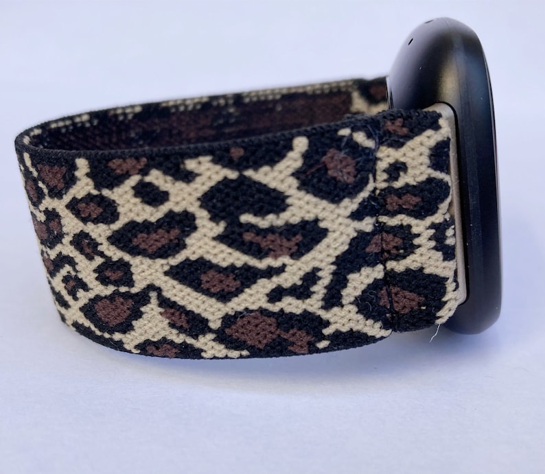 Puede incluir: Una banda de reloj el&aacute;stica de estampado de leopardo negro y marr&oacute;n con una esfera de reloj negra.