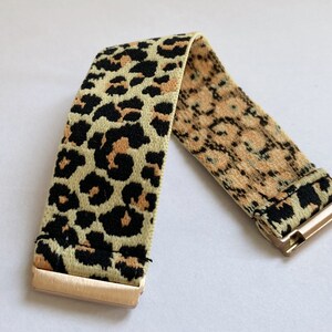 May include: A gold elastic bracelet with a leopard print pattern. The bracelet is made of a soft, stretchy material and has a gold clasp.