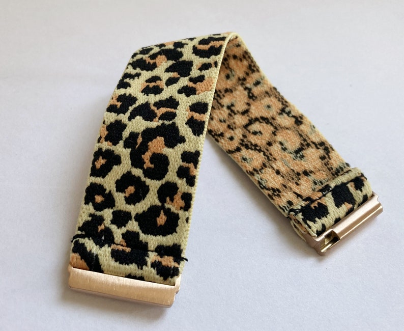 May include: A gold elastic bracelet with a leopard print pattern. The bracelet is made of a soft, stretchy material and has a gold clasp.