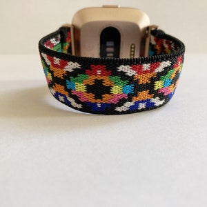 May include: A black and white patterned elastic watch band with rainbow colored accents. The band is designed to fit a smartwatch.