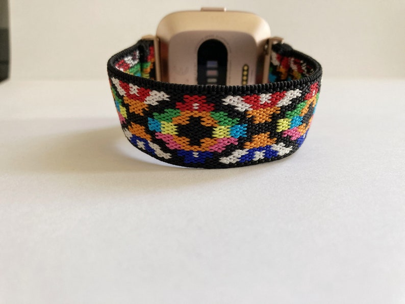 May include: A black and white patterned elastic watch band with rainbow colored accents. The band is designed to fit a smartwatch.
