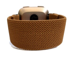 May include: A brown elastic watch band with a gold-colored watch face.