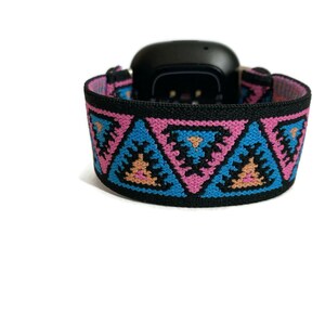 May include: A black watch band with a geometric pattern in pink, blue, and orange. The pattern features repeating triangles.