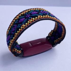 May include: A burgundy fitness tracker with a black and colorful patterned band. The band has a geometric design with orange, yellow, purple, and blue accents.