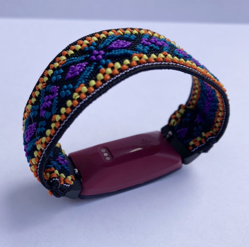 May include: A burgundy fitness tracker with a black and colorful patterned band. The band has a geometric design with orange, yellow, purple, and blue accents.