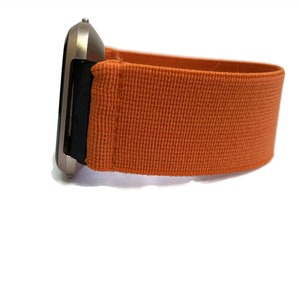 K&ouml;nnte beinhalten: Eine silberne Smartwatch mit einem orangefarbenen Stoffarmband. Das Armband ist aus gewebtem Material und hat eine glatte Textur.