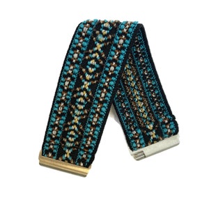 May include: A black elastic watch band with a turquoise, brown, and white geometric pattern. The band has gold and silver metal clasps.