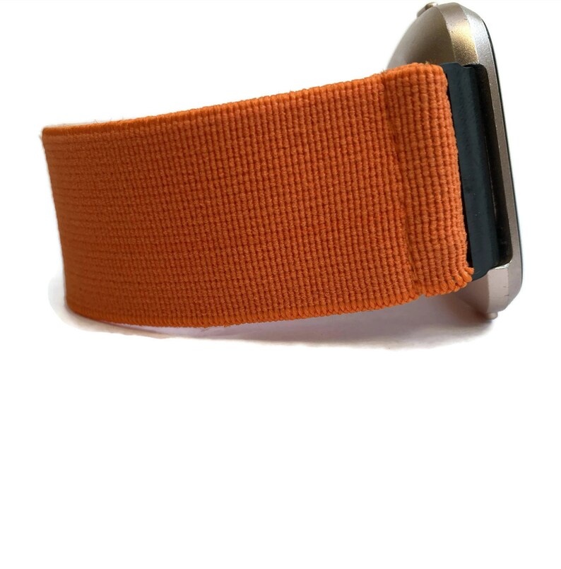 K&ouml;nnte beinhalten: Orangefarbenes Armband aus gewebtem Stoff. Das Armband ist an einem silbernen Zifferblatt befestigt.