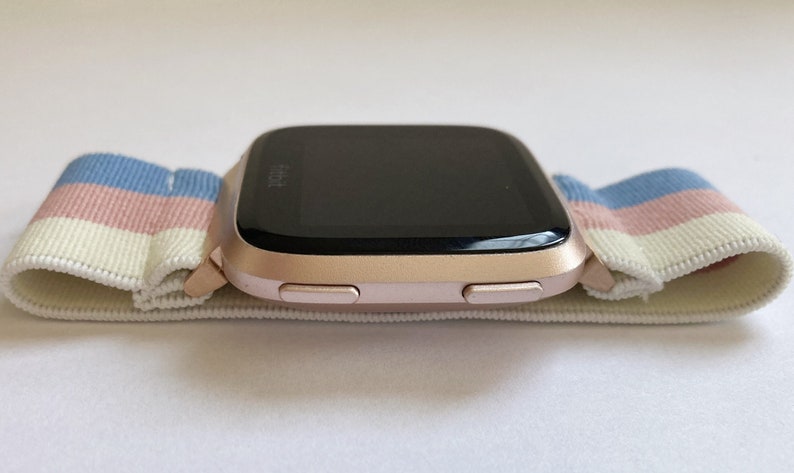 May include: A rose gold smartwatch with a black screen and two buttons on the side. The watch is on a white and blue striped elastic band.