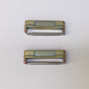 May include: Two gold-toned watch band spring bars with a silver finish. The spring bars are designed to connect a watch band to a watch case.