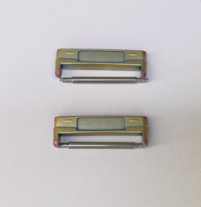 May include: Two gold-toned watch band spring bars with a silver finish. The spring bars are designed to connect a watch band to a watch case.