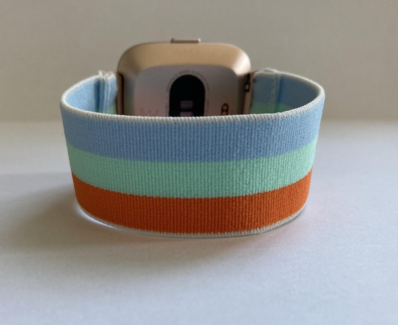May include: A gold-colored smartwatch with a blue, green, and orange striped elastic band.
