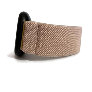 May include: A light pink elastic watch strap with a black metal buckle.