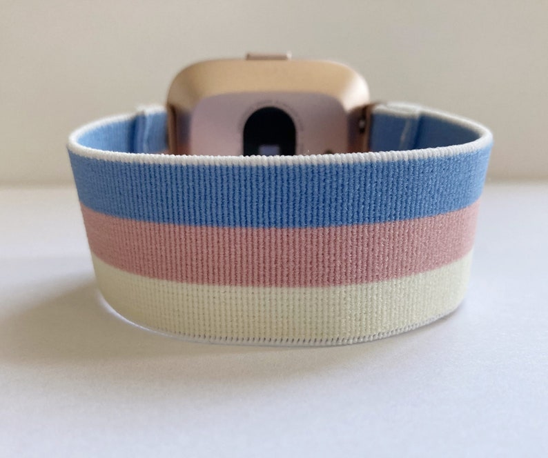 May include: A light blue, pink, and white striped elastic watch band. The band is made of a soft, stretchy material and is designed to fit comfortably on the wrist.