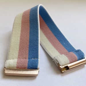 May include: A white, pink, and blue striped elastic band with gold metal clasps.