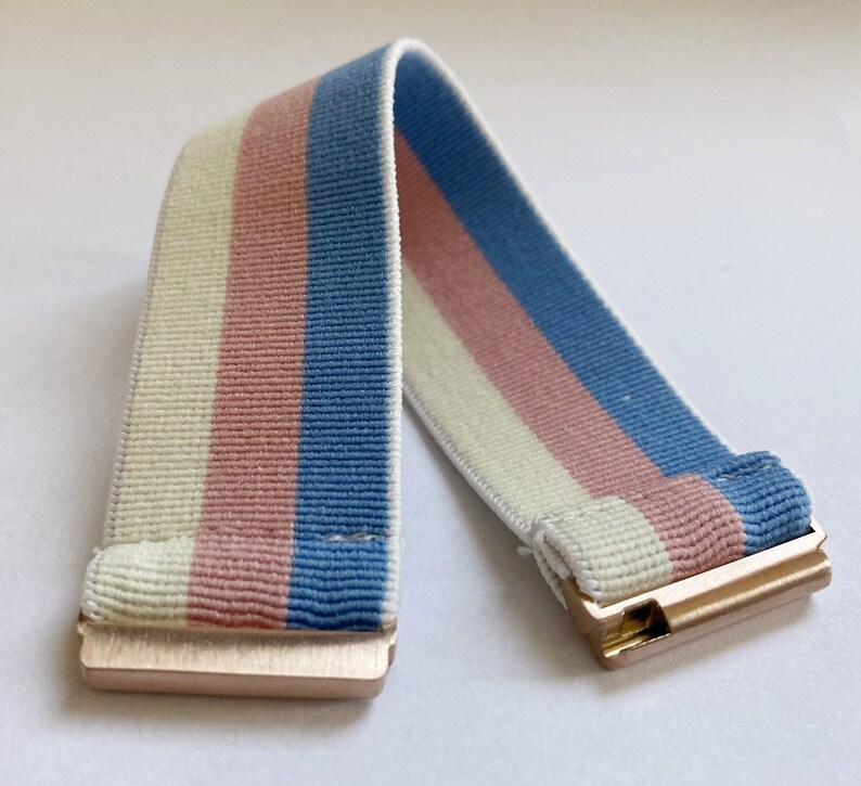 May include: A white, pink, and blue striped elastic band with gold metal clasps.