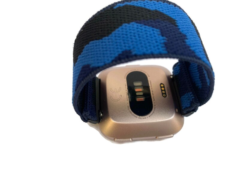 Op de afbeelding: Een smartwatch van ros&eacute;goud met een blauw en zwart camouflageband. Het horloge gezicht toont de tijd en datum.