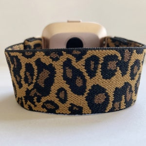 May include: A gold-colored fitness tracker with a leopard print elastic band.