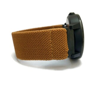 May include: A brown fabric watch band with a black watch face.