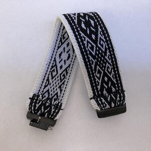 Peut inclure: Un bracelet de montre &agrave; motifs noirs et blancs avec un motif g&eacute;om&eacute;trique. Le bracelet est fait de tissu tiss&eacute; et comporte des connecteurs en plastique noir &agrave; chaque extr&eacute;mit&eacute;. Le bracelet est pli&eacute; en forme de V.