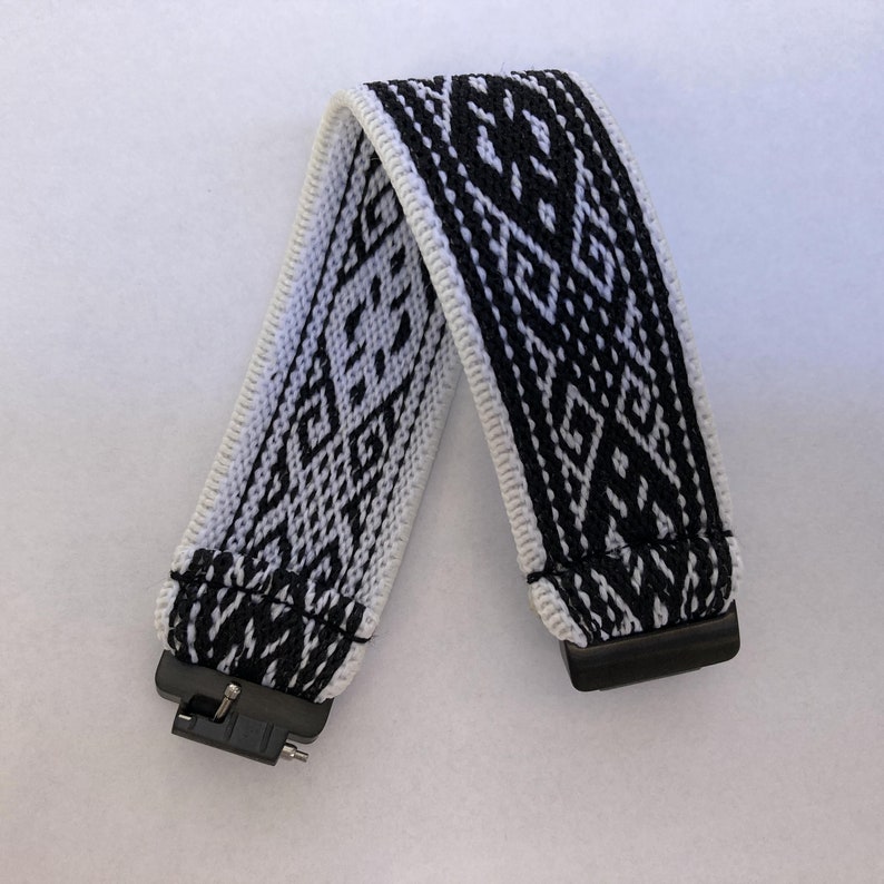 Peut inclure: Un bracelet de montre &agrave; motifs noirs et blancs avec un motif g&eacute;om&eacute;trique. Le bracelet est fait de tissu tiss&eacute; et comporte des connecteurs en plastique noir &agrave; chaque extr&eacute;mit&eacute;. Le bracelet est pli&eacute; en forme de V.