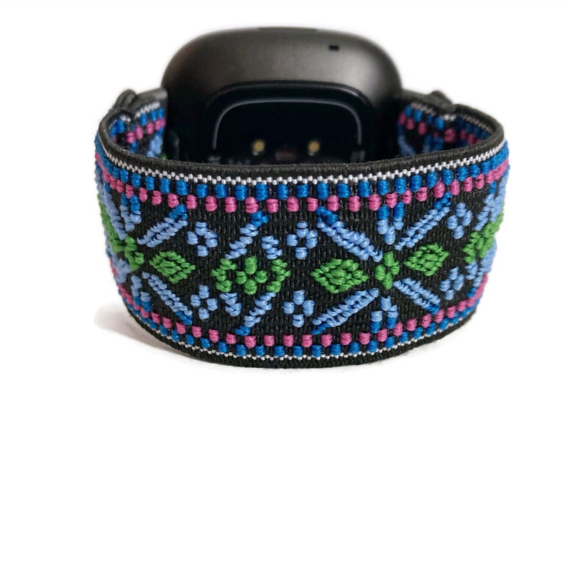May include: Black fitness tracker with a colourful patterned elastic band. The band features a geometric design with blue, green, and pink accents.