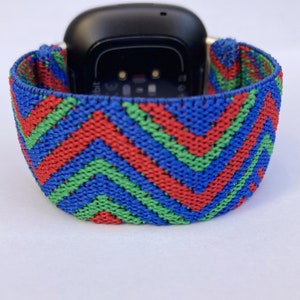 May include: A red, green, and blue patterned elastic watch band for a Fitbit smartwatch.