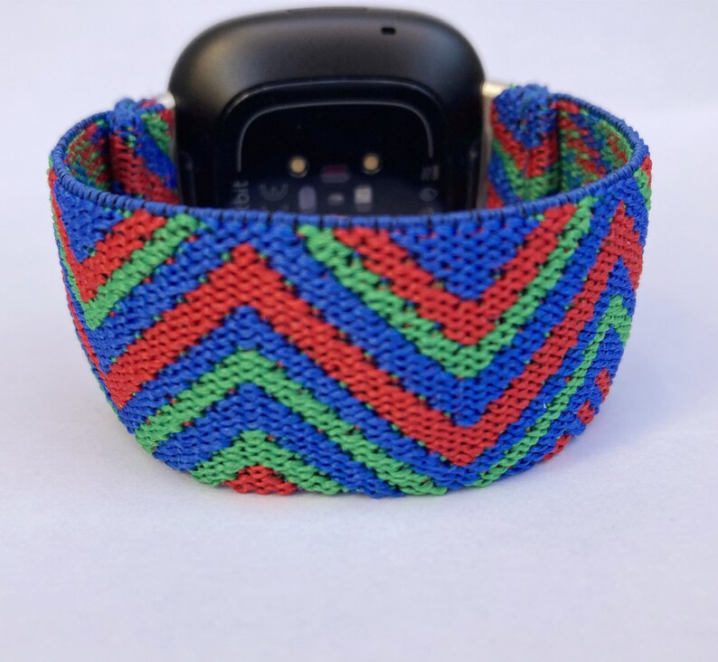 May include: A red, green, and blue patterned elastic watch band for a Fitbit smartwatch.