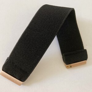 May include: A black elastic band with gold metal clasps. The band is folded in half and the clasps are visible.