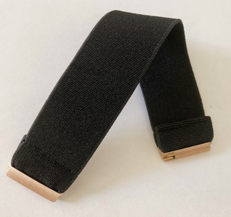 May include: A black elastic band with gold metal clasps. The band is folded in half and the clasps are visible.