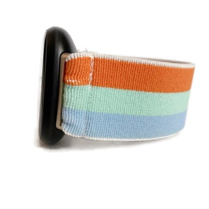 May include: A striped watch band with orange, light blue and light green stripes. The band is made of a soft, stretchy material.