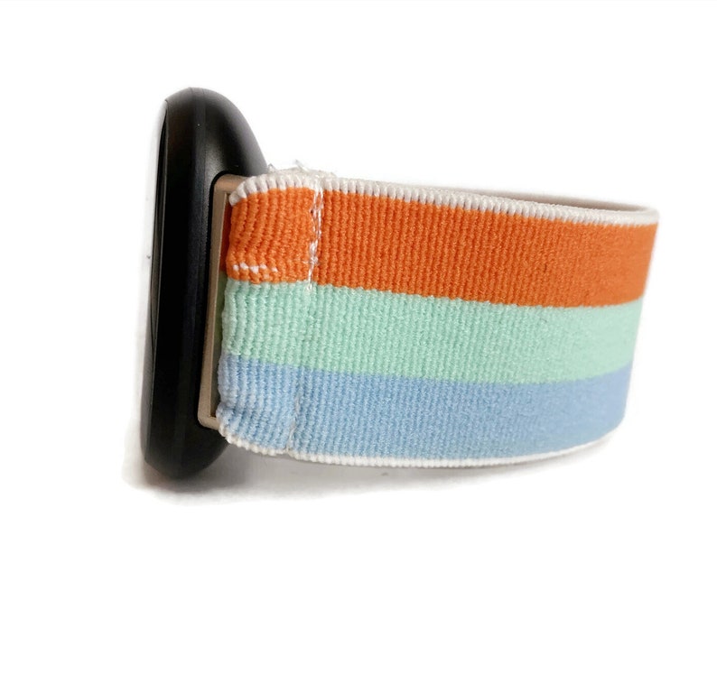 May include: A striped watch band with orange, light blue and light green stripes. The band is made of a soft, stretchy material.