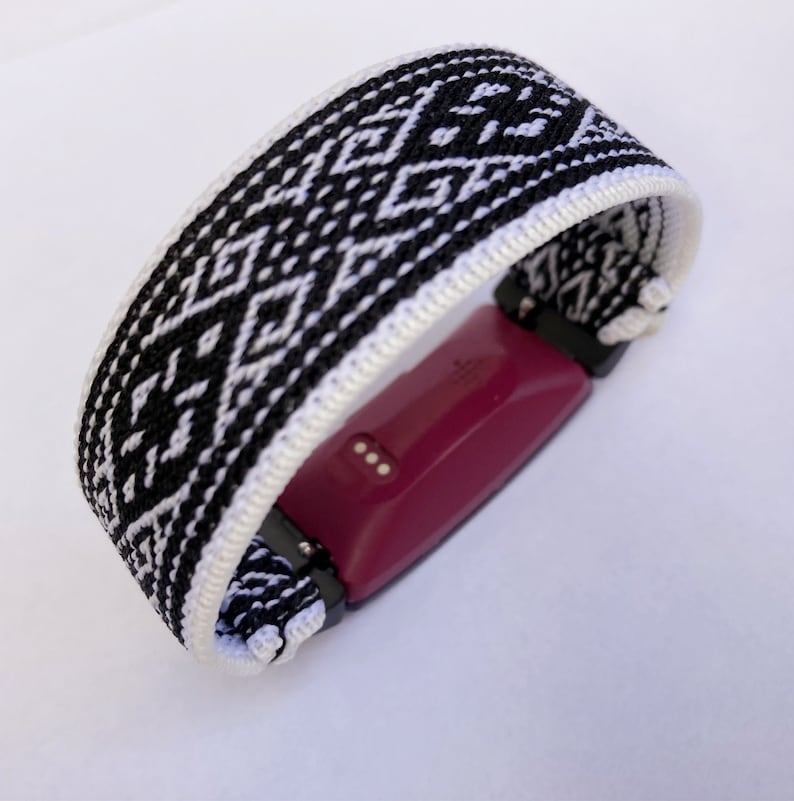 Peut inclure: Bracelet de montre tiss&eacute; &agrave; motifs noirs et blancs. Le bracelet pr&eacute;sente un motif g&eacute;om&eacute;trique et est enroul&eacute; autour d'un tracker de fitness bordeaux. Le bracelet mesure environ 2,5 cm de large.