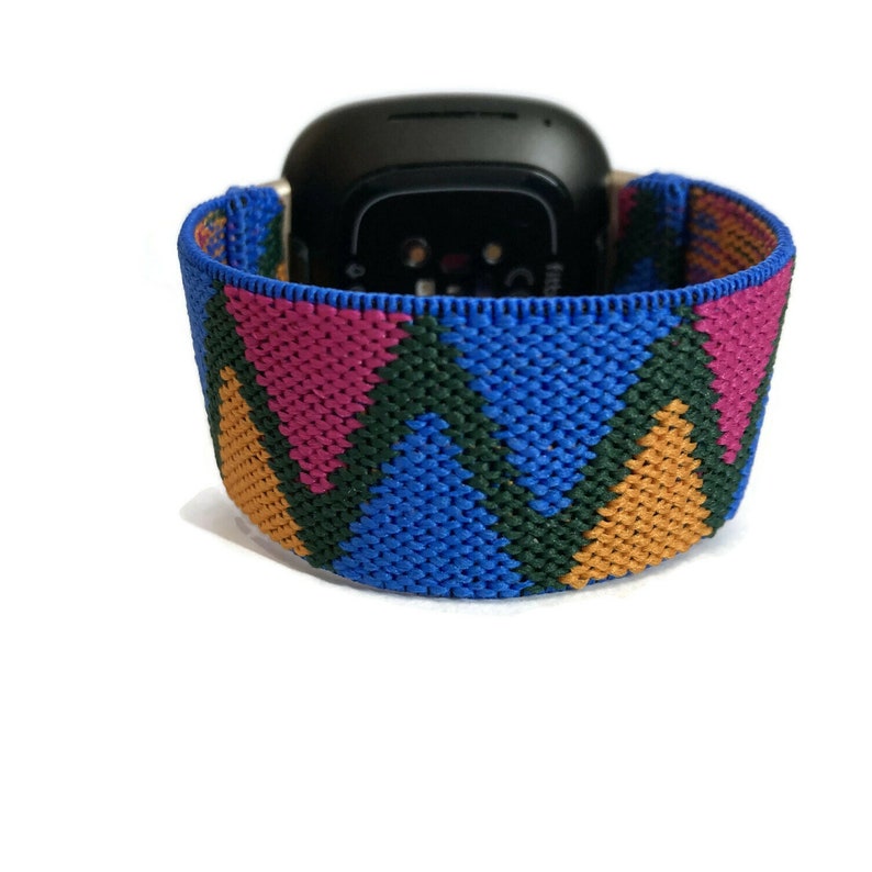 May include: A colorful geometric patterned watch band in blue, green, pink, and orange. The band is made of woven elastic material.