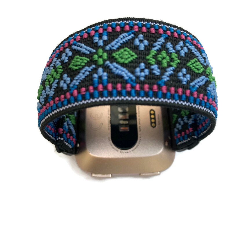 May include: A black and blue patterned watch band with a gold smartwatch. The band has a geometric design with green, blue, and pink accents.