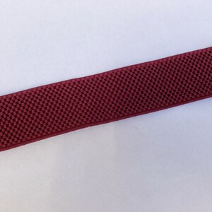 May include: A maroon elastic watch band with silver metal clasps.