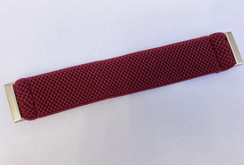 May include: A maroon elastic watch band with silver metal clasps.