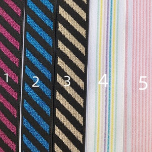 May include: Five samples of elastic trim with different patterns. Sample 1 is black with pink diagonal stripes. Sample 2 is black with blue diagonal stripes. Sample 3 is black with gold diagonal stripes. Sample 4 is white with multi-colored vertical stripes. Sample 5 is white with pink vertical stripes.